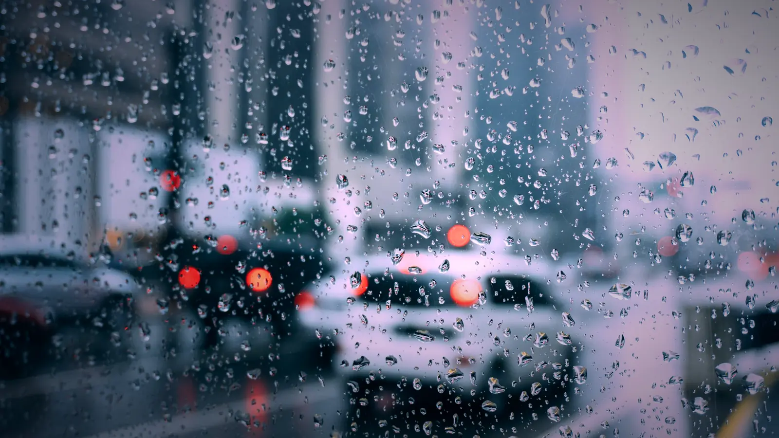 Raindrops on a windshield overlooking a quiet night street with soft red and amber lights