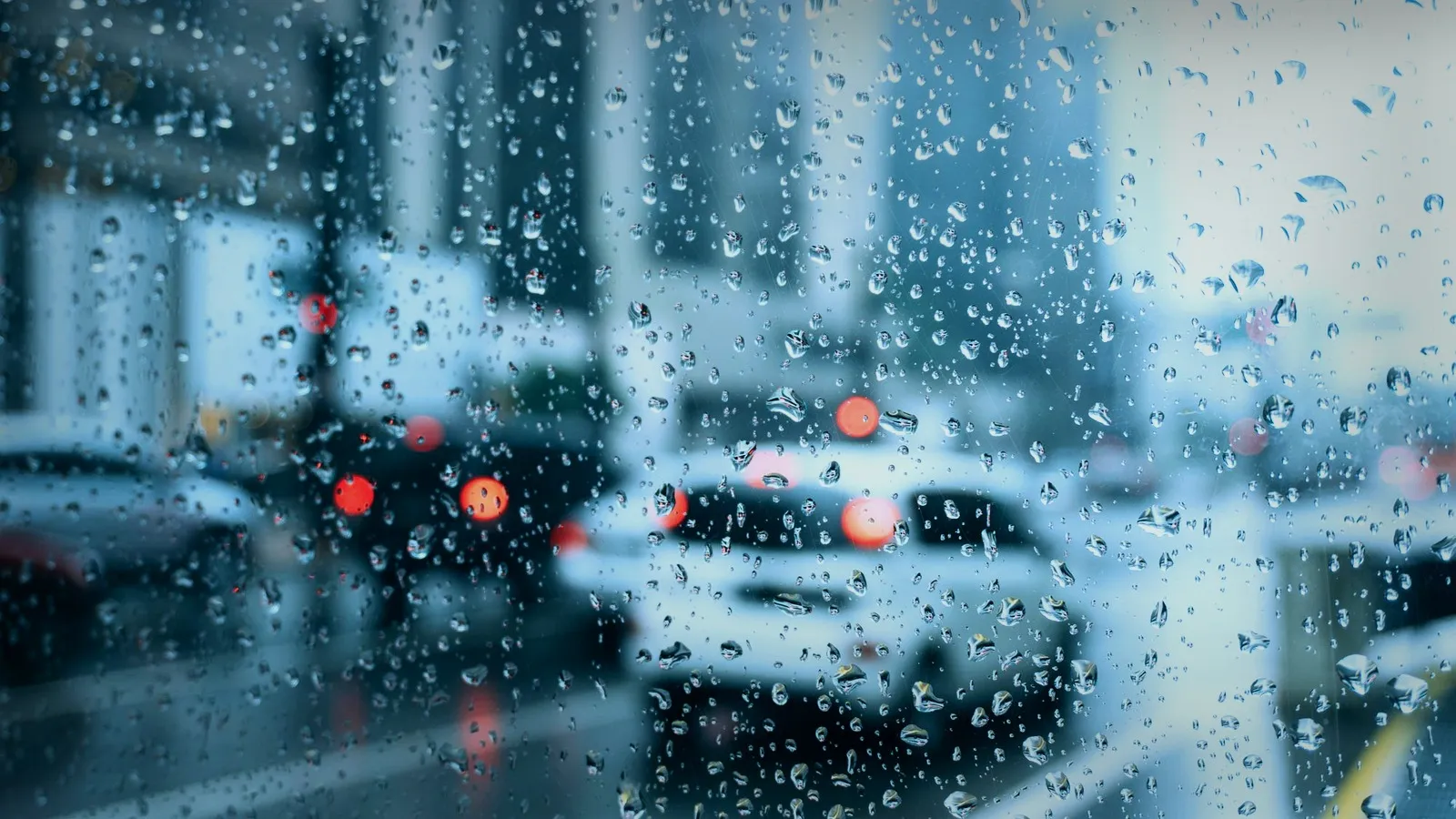 Raindrops on a windshield overlooking a quiet night street with soft red and amber lights