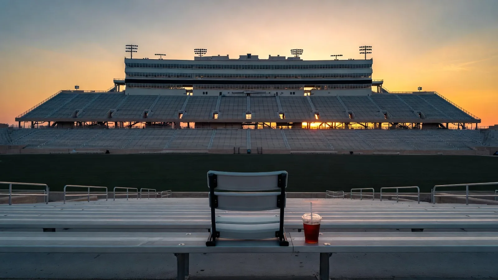 Empty college stadium at dusk with a lone seat cushion and soda cup on the bleacher steps